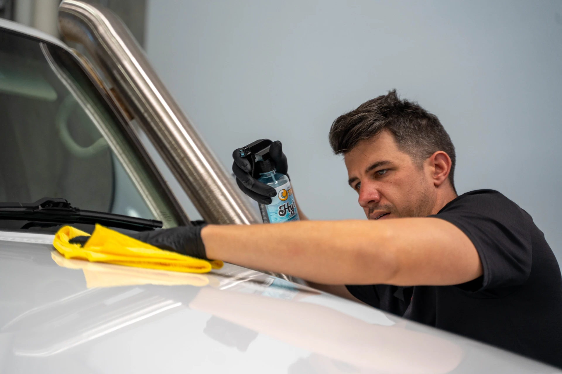Detailer applying a hybrid ceramic spray to a white vehicle before sale