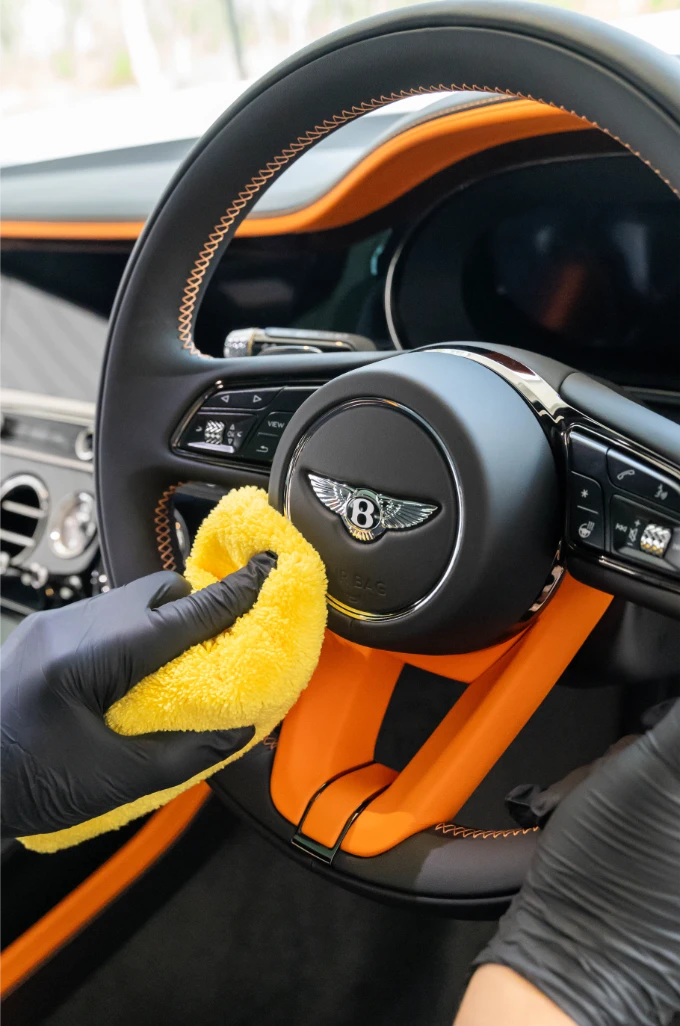 Detailer wiping down a Bentley steering wheel during an interior detail
